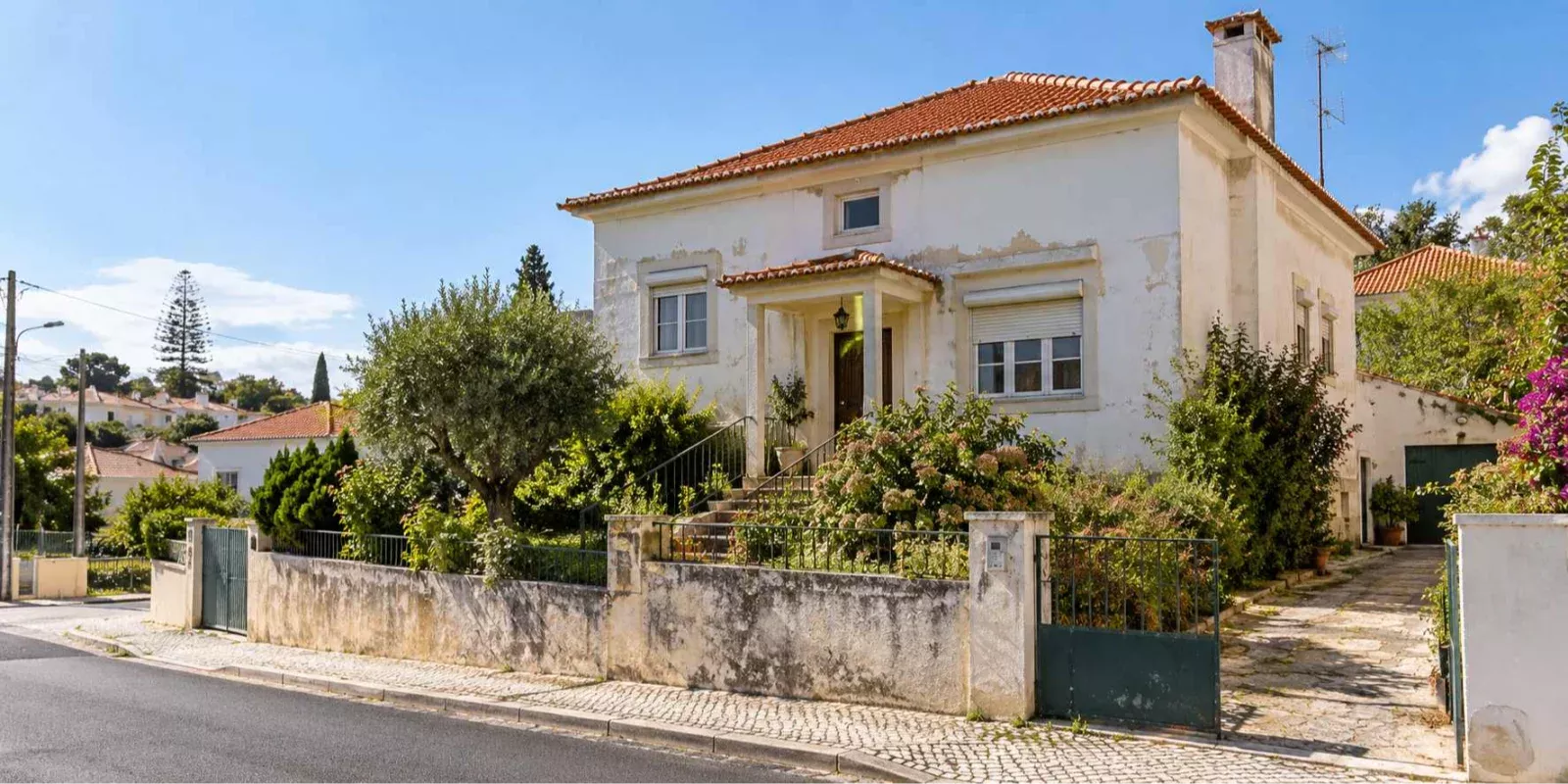 Moradia antiga de dois pisos, com fachada desgastada e jardim, ilustrando uma casa herdada que necessita de remodelação em Alcabideche, Cascais.
